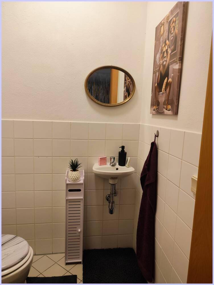 Kleines Gäste-WC mit weißen Fliesen, ovalem Spiegel und modernem Waschbecken.
