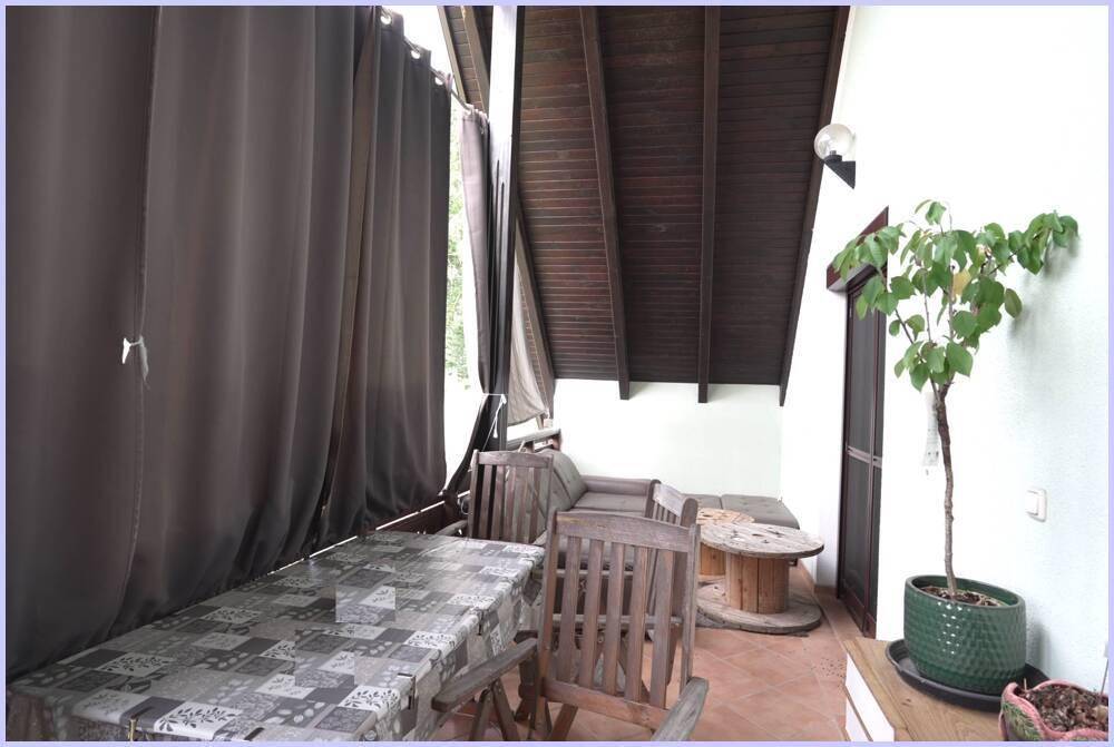 Überdachter Balkon mit Holzboden, Sitzgelegenheiten und Vorhängen für Privatsphäre.