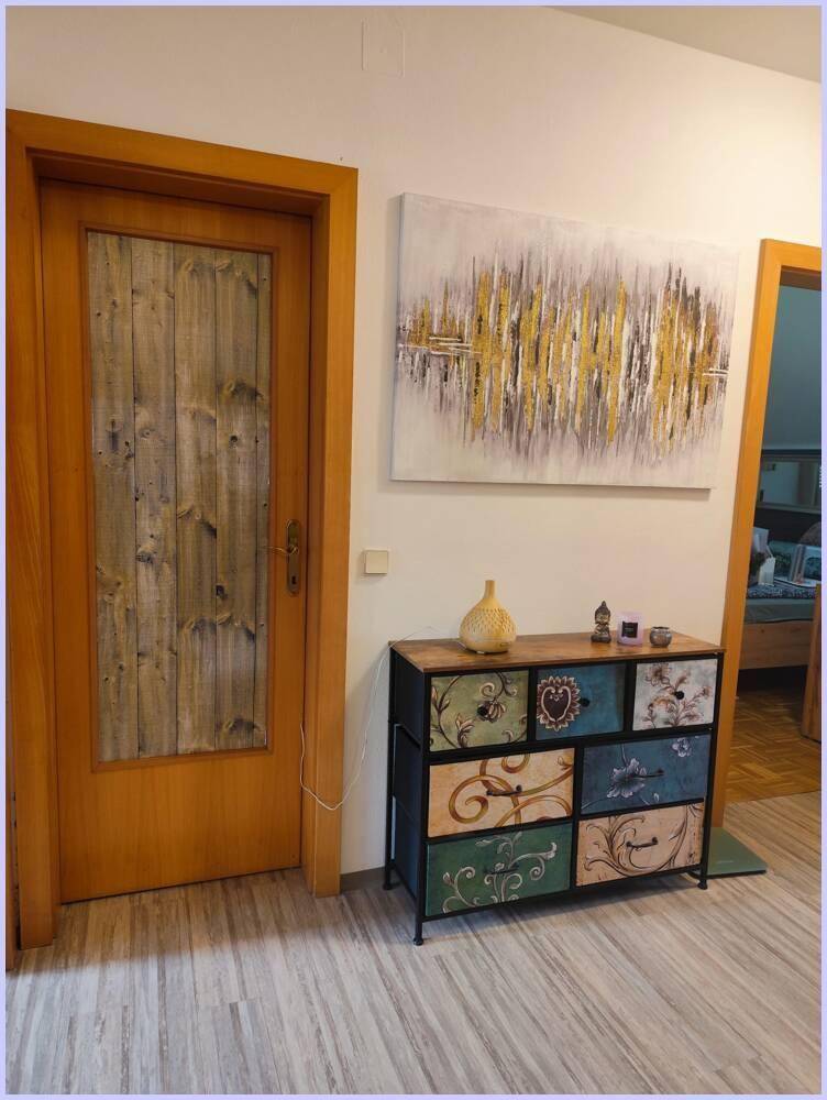 Heller Flur mit Holztür, dekorativer Kommode und abstrakter Kunst an der Wand.