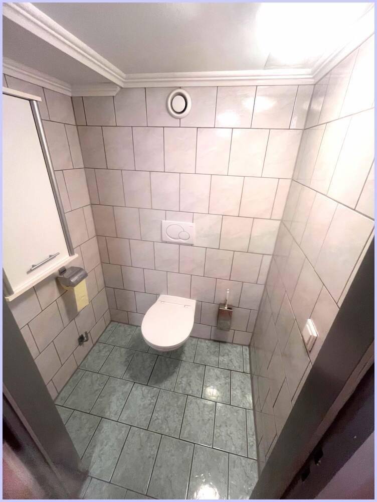Einfaches Gäste-WC mit Wand-WC, Fliesen und Abluftventilator.