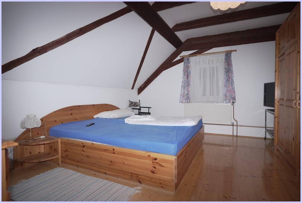 Helles Schlafzimmer im Dachgeschoss mit Holzboden, sichtbaren Holzbalken und einem Fenster für Tageslicht.