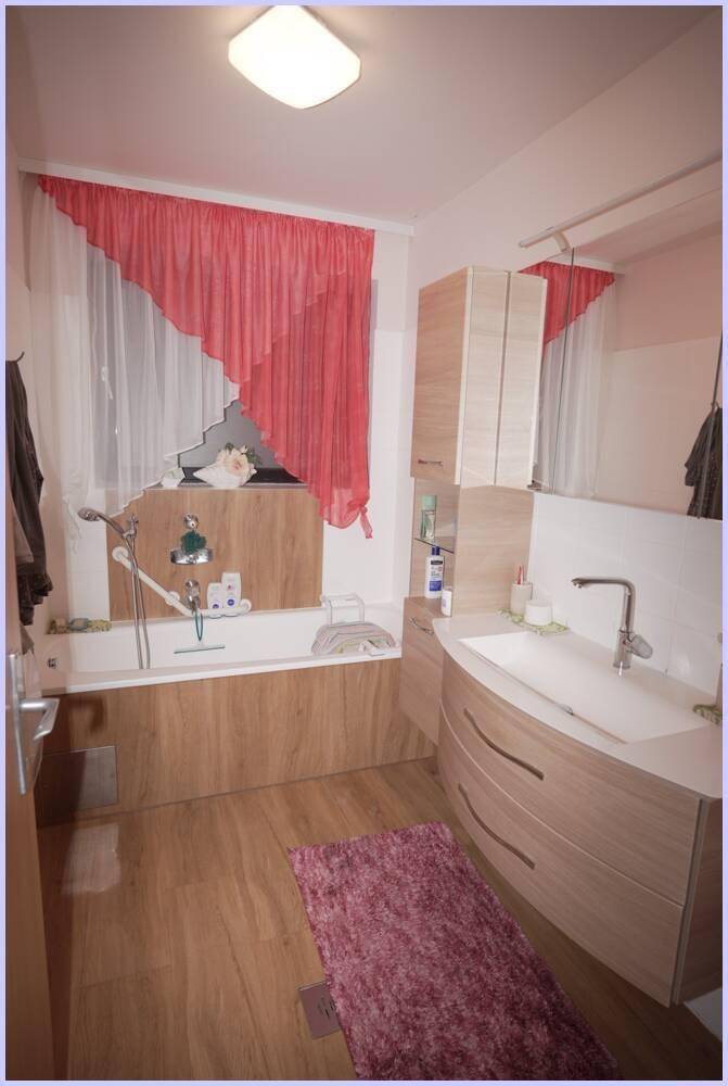 Modernes Badezimmer mit Badewanne, Holzverkleidung und rotem Vorhang am Fenster.