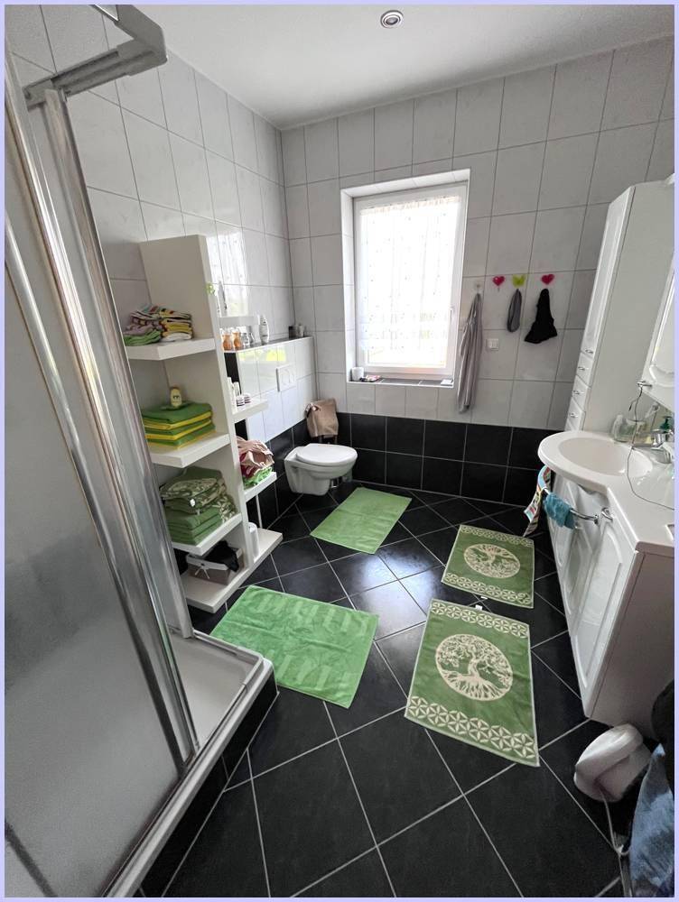Helles Badezimmer mit Duschkabine, WC und Fenster, dekoriert mit grünen Badematten.