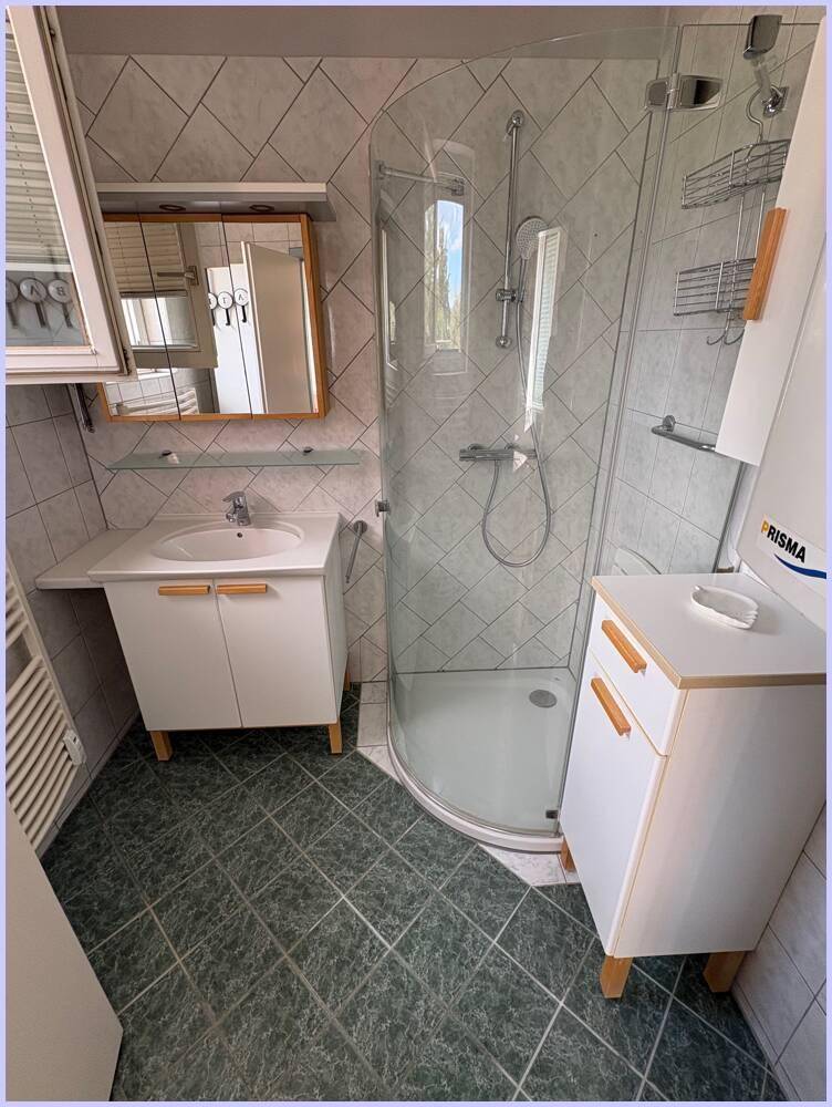 Helles Badezimmer mit Duschkabine, Waschbecken und praktischen Ablagemöglichkeiten.