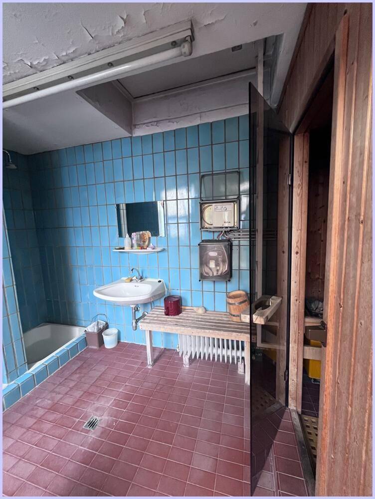 Badezimmer mit blauen Wandfliesen, rotem Boden und direktem Zugang zu einer Holzsauna.
