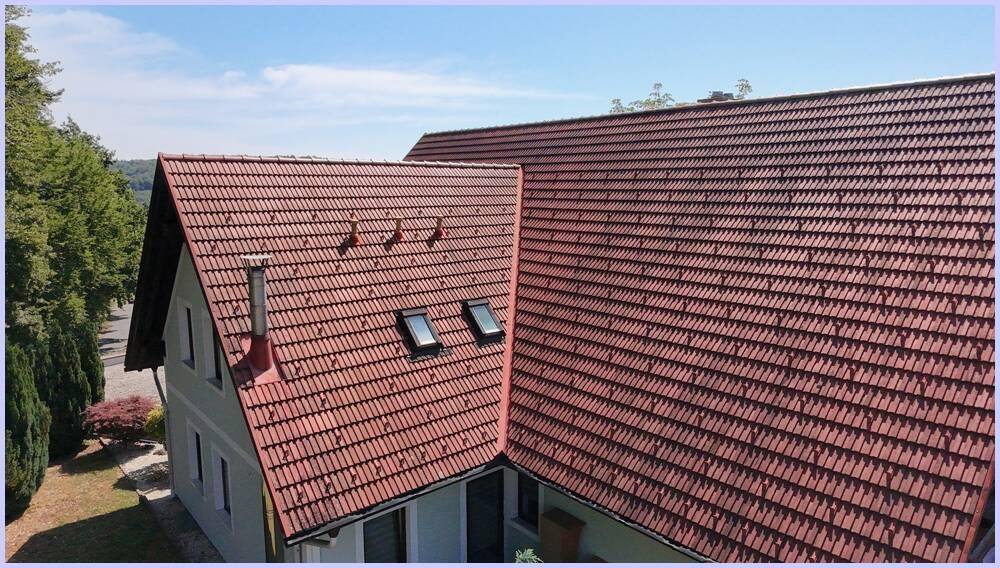 Dachansicht eines Hauses mit roten Ziegeln, Schornstein und mehreren Dachfenstern.
