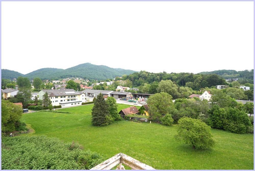 Panoramablick über ein grünes Tal mit Häusern und Bergen unter hellem Himmel.