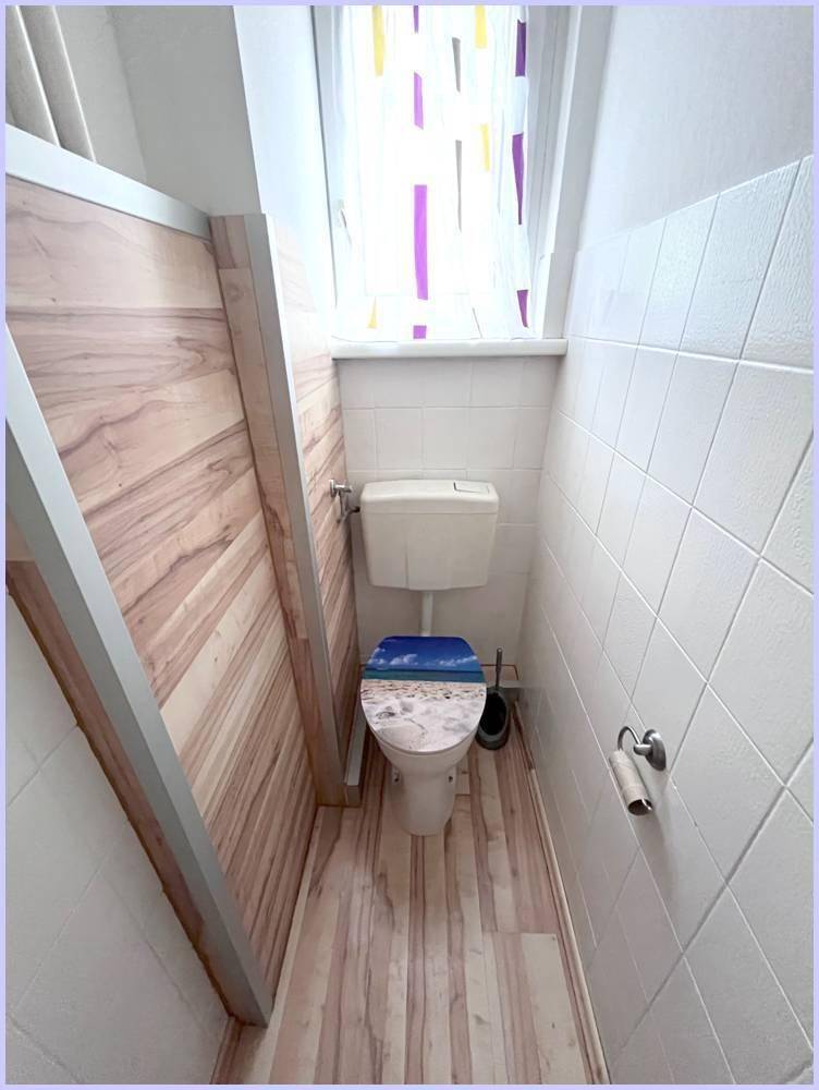 Kleines WC mit Fenster, weiß gefliesten Wänden und Holzboden.