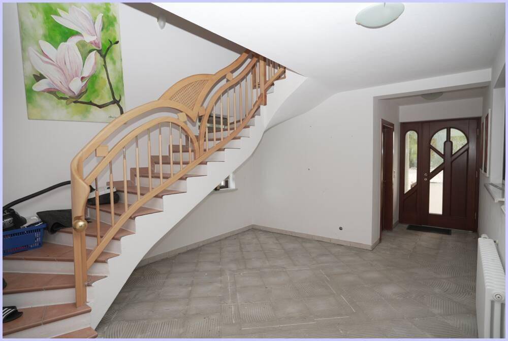Geräumiger Eingangsbereich mit geschwungener Holztreppe und Fliesenboden.