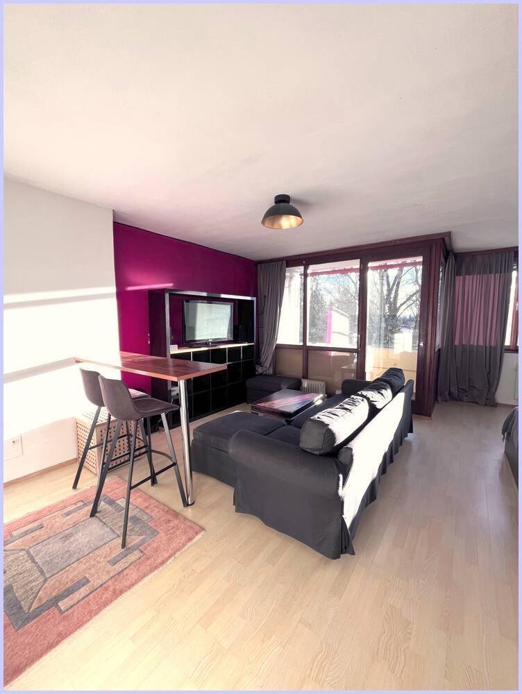 Offener Wohnbereich mit Sofa, Fernseher und einer kleinen Bar, akzentuiert durch eine lila Wand.