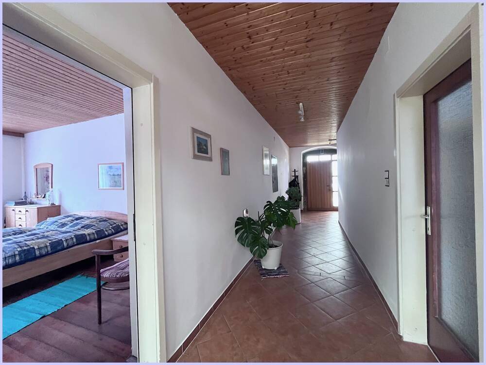 Langer Flur mit Terrakottafliesen, Holzdecke und Blick in ein angrenzendes Schlafzimmer.