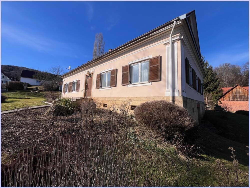 Seitenansicht des Haupthauses mit traditioneller Architektur, Fensterläden und einem leicht erhöhten Grundstück.