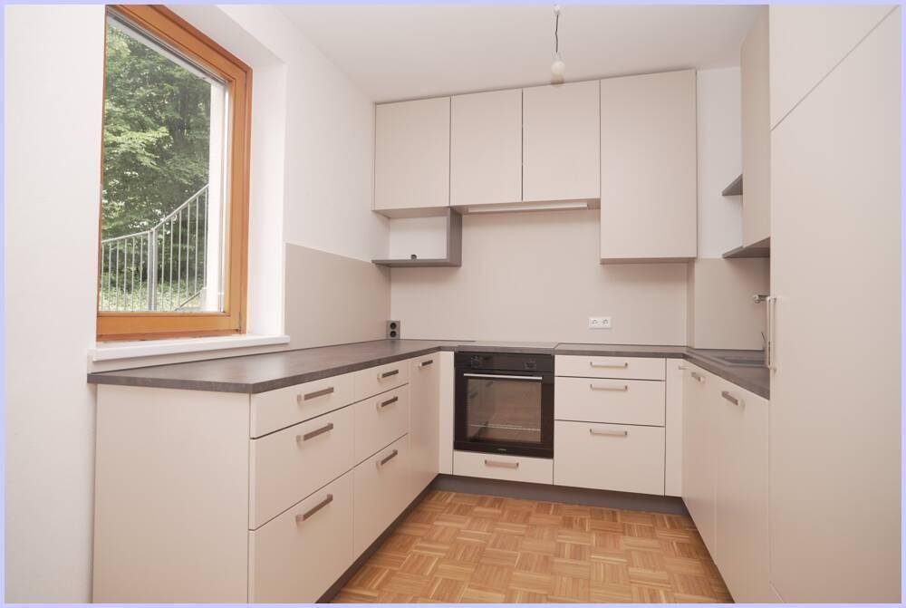 Moderne Küche mit hellen Fronten, integriertem Backofen und Fenster mit Blick ins Grüne.