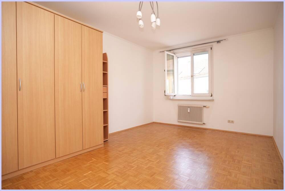 Schlafzimmer mit großem Kleiderschrank, Parkettboden und Fenster.
