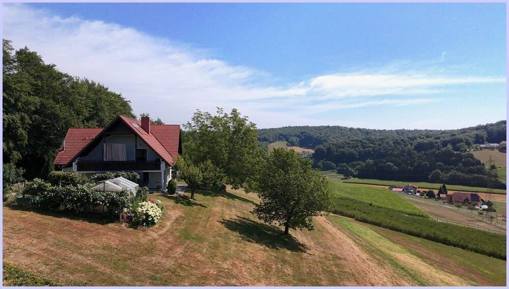 Haus mit rotem Dach und hellgrüner Fassade, eingebettet in eine weite grüne Landschaft unter blauem Himmel.
