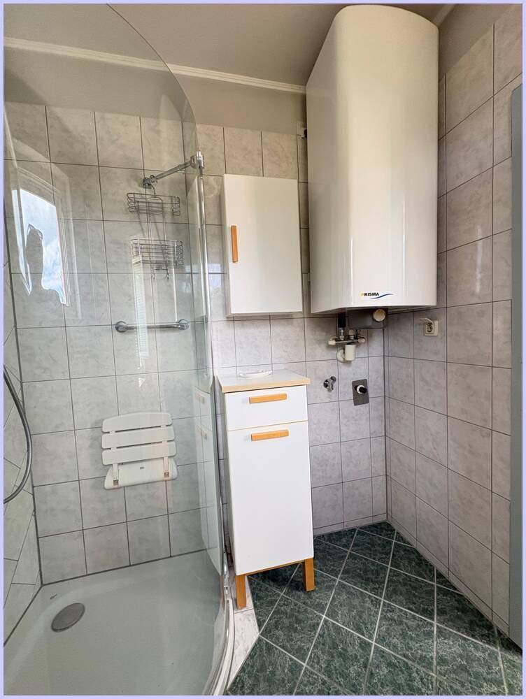 Duschbereich mit Sitzgelegenheit, Haltegriffen und Warmwasserboiler.