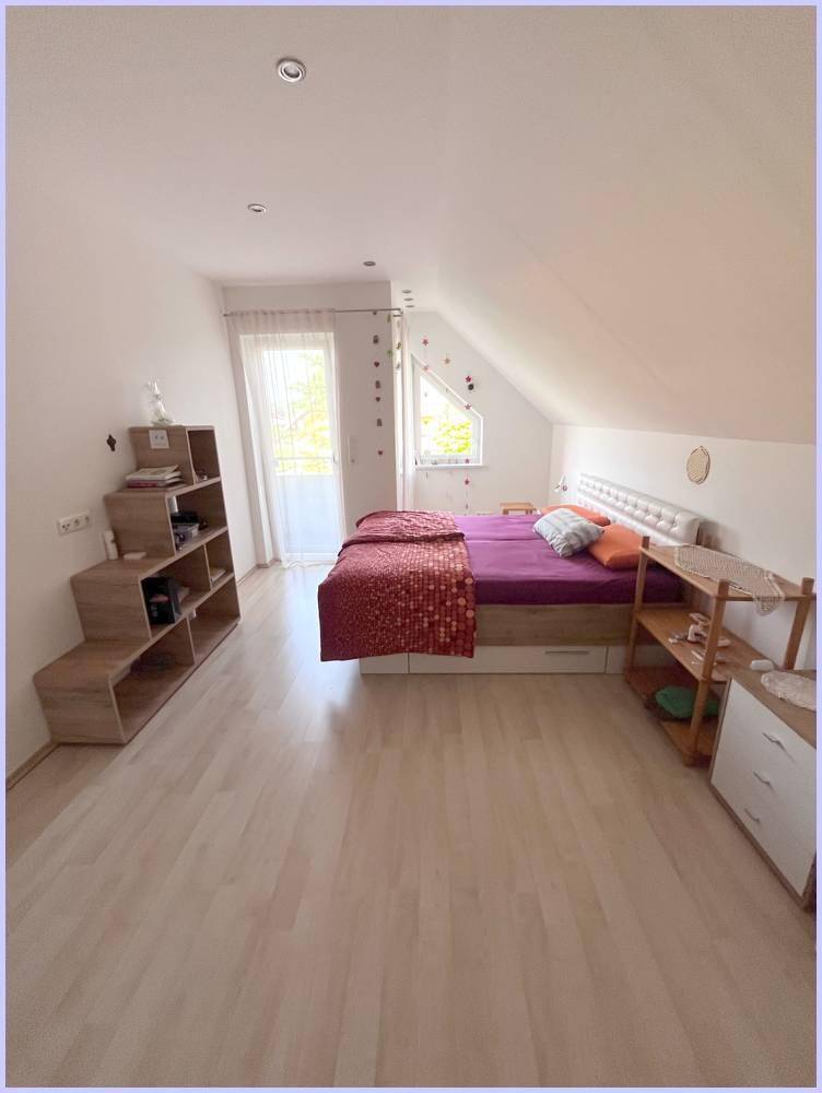 Helles Schlafzimmer im Dachgeschoss mit Bett, Regalen und schrägen Decken.
