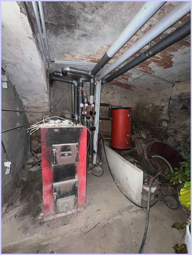 Heizraum im Keller mit einem alten Holzofen und Rohren, die die Heizungsanlage bilden.