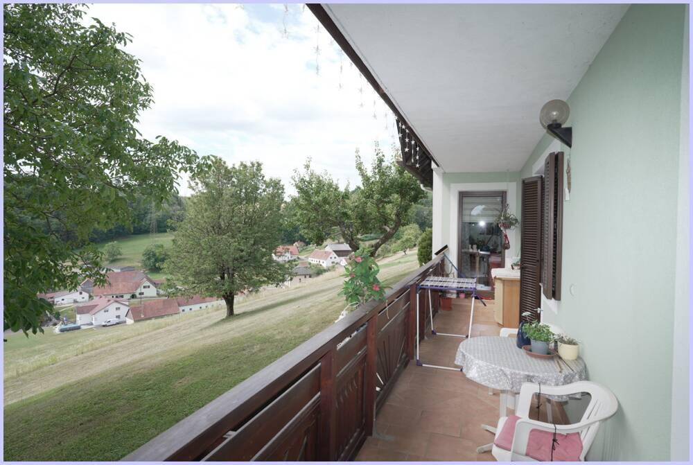 Geräumiger Balkon mit Holzboden und Möbeln, ideal zum Entspannen mit Blick auf die ländliche Umgebung.