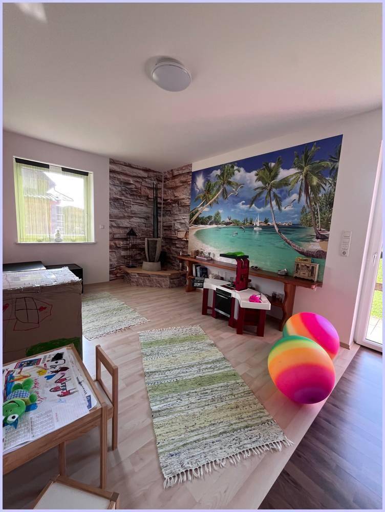 Wohnbereich mit tropischer Wandtapete, Holzwand und Spielbereich für Kinder.