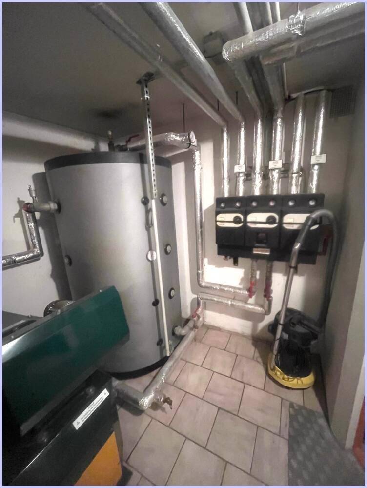 Heizungsraum mit Warmwasserspeicher, Rohren und Staubsauger.
