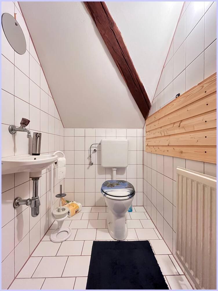 Separate Toilette im Dachgeschoss mit weißen Fliesen, kleinem Waschbecken und Dachschräge.