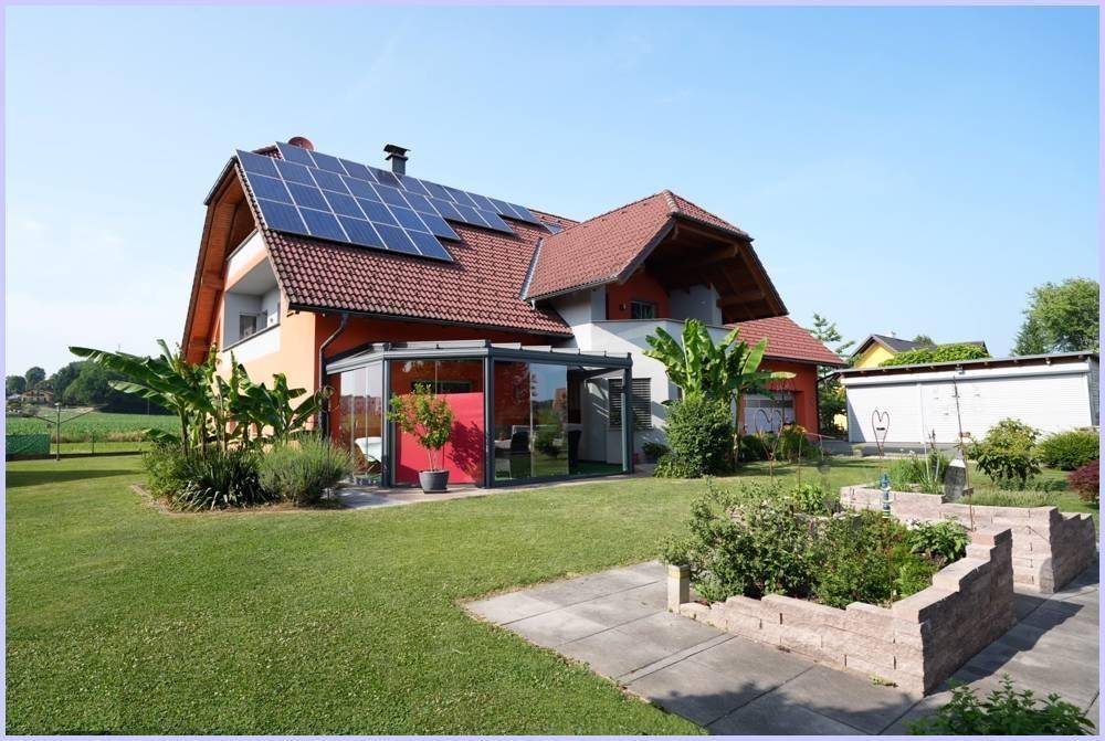 Seitenansicht des Hauses mit Wintergarten, gepflegtem Rasen und einem kleinen Kräutergarten.