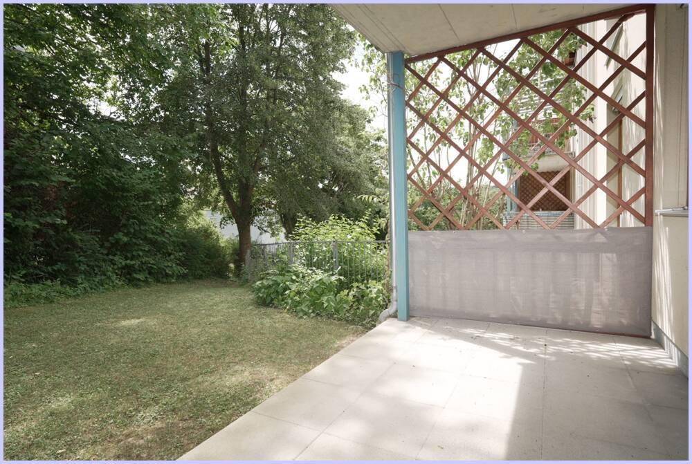 Grüner Gartenbereich mit Rasenfläche und angrenzender Terrasse, umgeben von Bäumen.