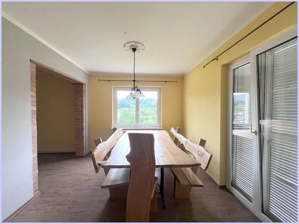 Geräumiger Essbereich mit großem Holztisch und Fenster mit Blick ins Grüne.