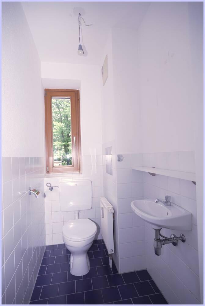 Separates WC mit Fenster, Toilette und kleinem Waschbecken, hell gefliest.