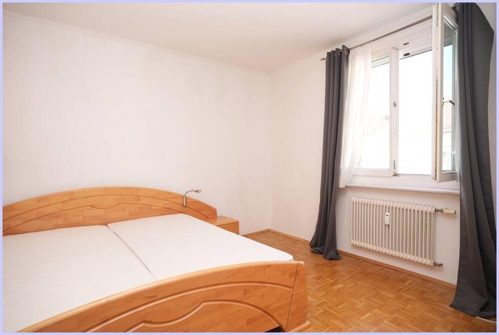 Gemütliches Schlafzimmer mit Holzbett, Parkettboden und Fenster mit Vorhängen.