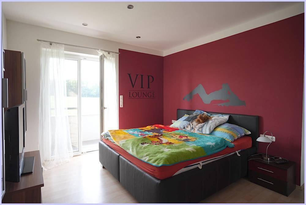 Schlafzimmer mit roter Akzentwand, Doppelbett und Zugang zu einem Balkon.