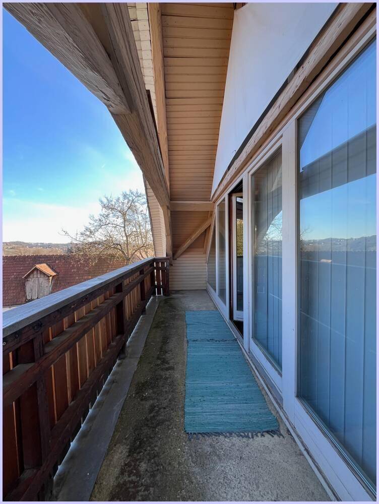 Langer Balkon mit Holzgeländer und weitem Blick auf die Umgebung unter blauem Himmel.