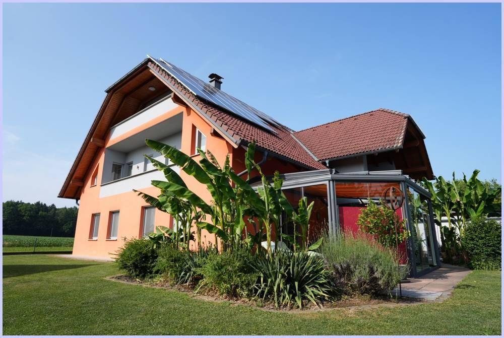 Ansicht des Hauses von der Seite mit Wintergarten, üppiger Bepflanzung und weitem Blick ins Grüne.