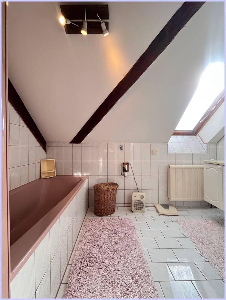 Badezimmer im Dachgeschoss mit Badewanne, weißen Fliesen und Dachfenster für natürliches Licht.