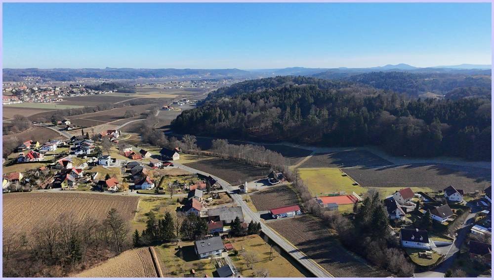 Panoramablick aus der Luft auf ein Tal mit einem Dorf, Feldern und bewaldeten Hängen.