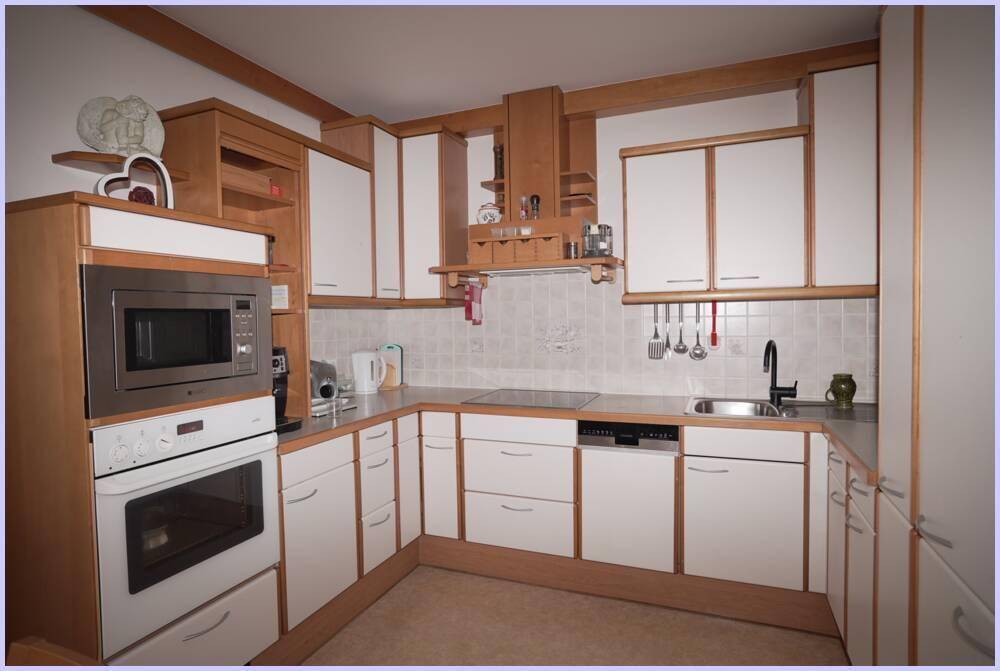 Funktionale Einbauküche mit hellen Fronten und Holzrahmen, ausgestattet mit modernen Geräten und Fliesenrückwand.