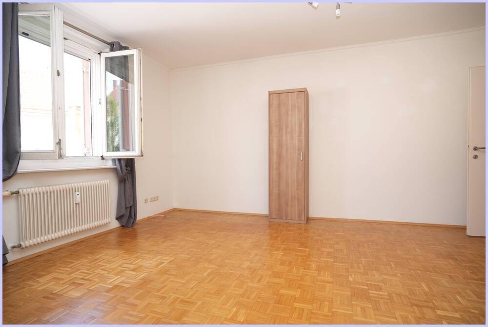 Helles Wohnzimmer mit Parkettboden und einem Fenster, das viel Tageslicht hereinlässt.
