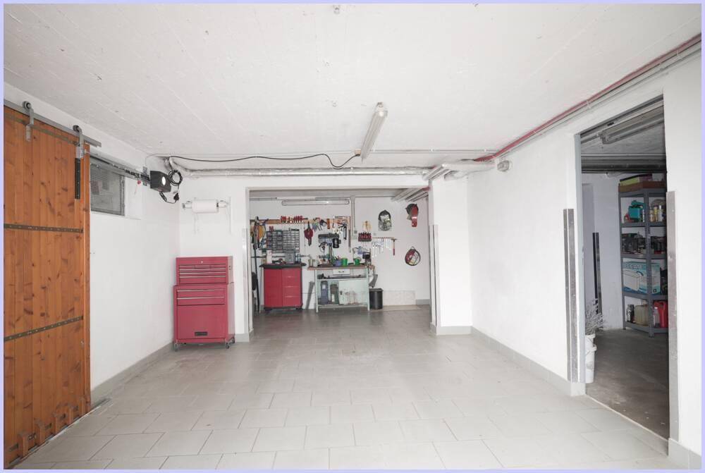 Geräumige Garage mit Fliesenboden, Werkbank und rotem Werkzeugschrank im Hintergrund.