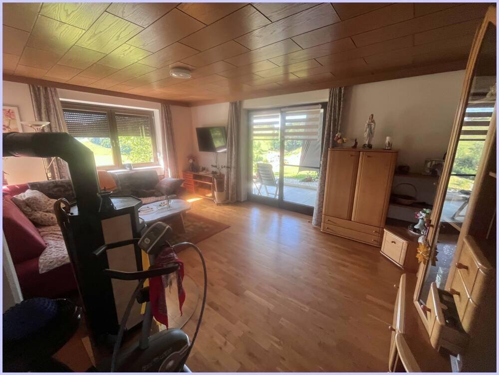 Helles Wohnzimmer mit Holzboden und Zugang zur Terrasse, bietet viel Tageslicht und Blick ins Grüne.