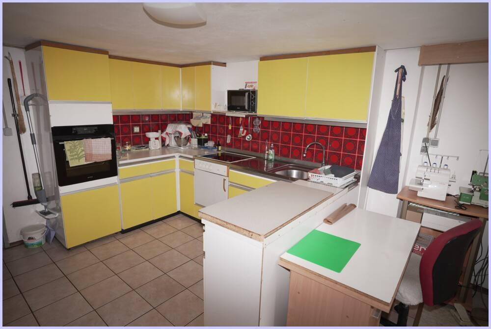 Funktionale Kellerküche mit gelben Fronten, rotem Fliesenspiegel und integriertem Backofen.