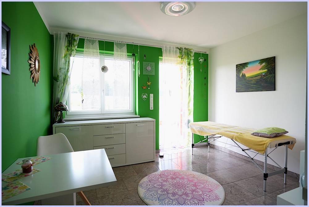 Freundliches Arbeitszimmer mit grünen Wänden, Fenster und einer Massageliege.