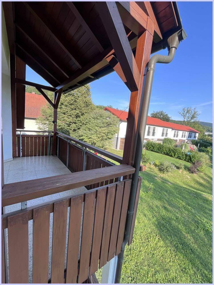 Überdachter Balkon mit Holzkonstruktion und Blick auf die grüne Umgebung und weitere Gebäude.