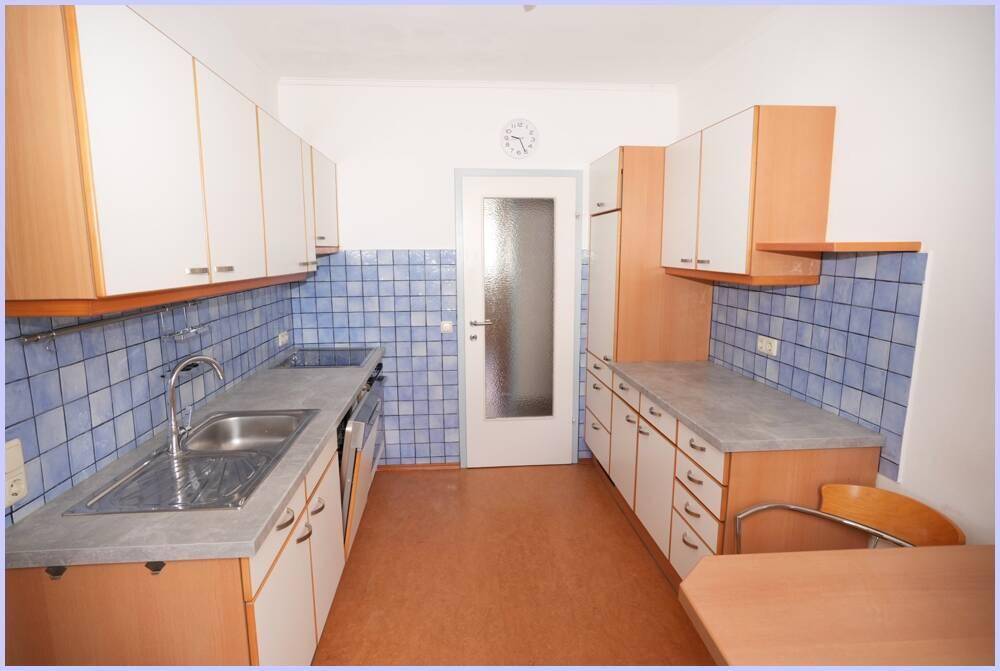 Funktionale Küche mit blauen Fliesen, weißen Schränken und Essbereich.