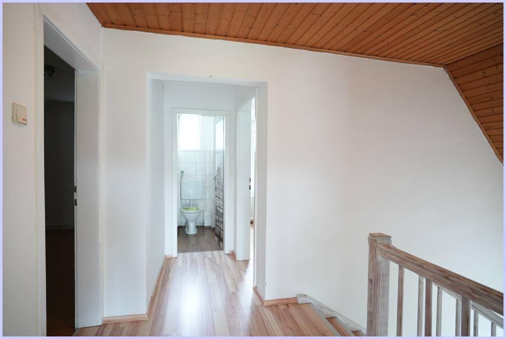 Heller Flur mit Holzdecke und Blick in ein kleines WC mit Fliesenboden.