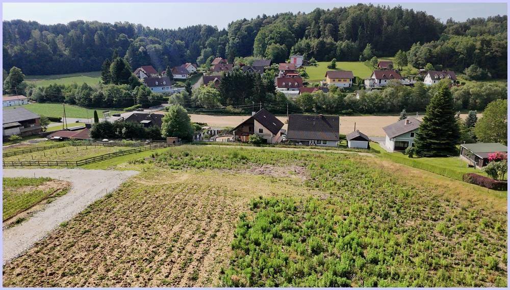 Luftbild einer offenen Landschaft mit Ackerflächen, Wiesen und einem kleinen Dorf am Horizont.