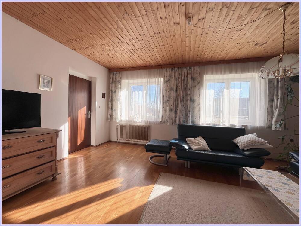 Helles Wohnzimmer mit Holzboden, Holzdecke und einem Sofa, das von Tageslicht durchflutet wird.