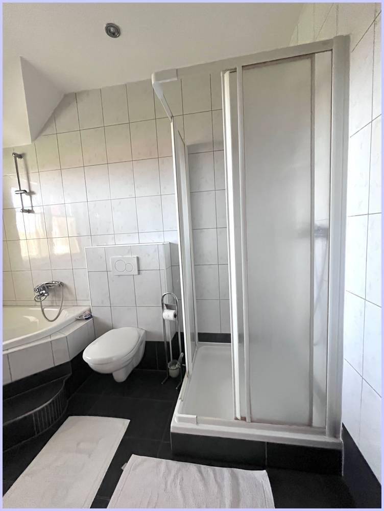 Badezimmer mit weißen und dunklen Fliesen, Duschkabine und integrierter Badewanne.