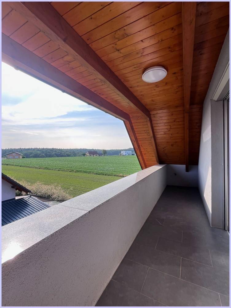 Überdachter Balkon mit Holzbalkendecke und weitem Blick über grüne Felder.