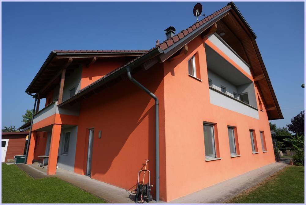 Detailansicht der Hausfassade in Orange mit Balkon und Dachüberstand.